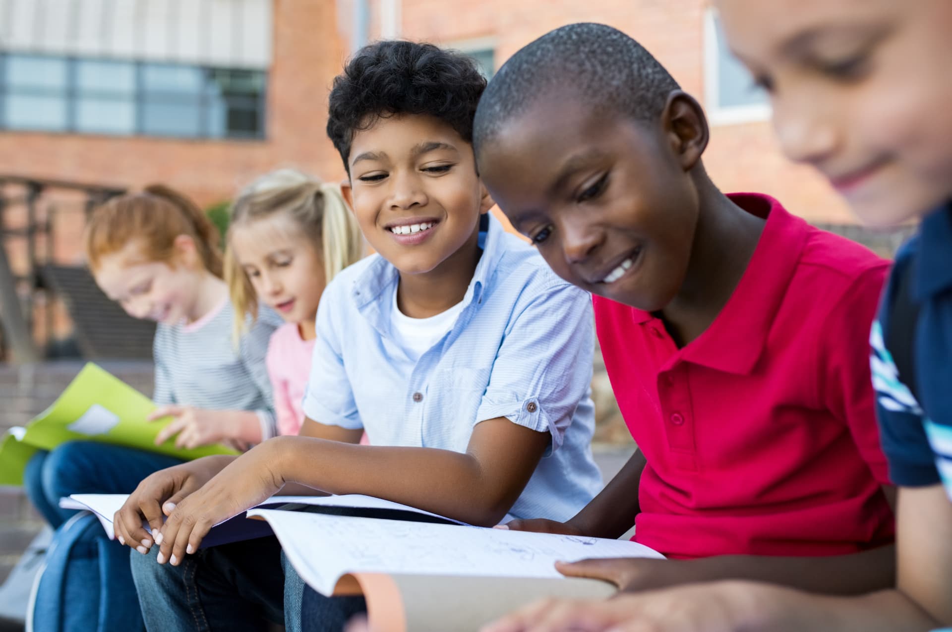 Elementary students smiling while reading books together outside