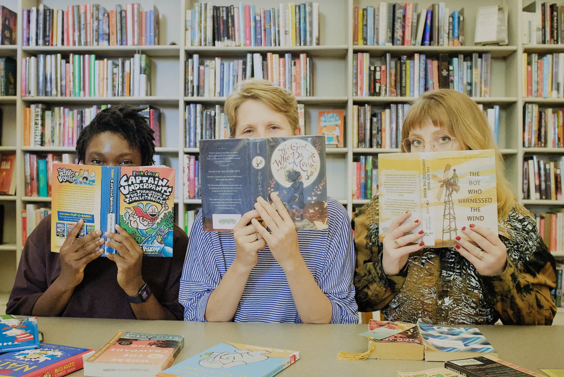 The M.A.R.S. co-founders holding books over their faces in a library